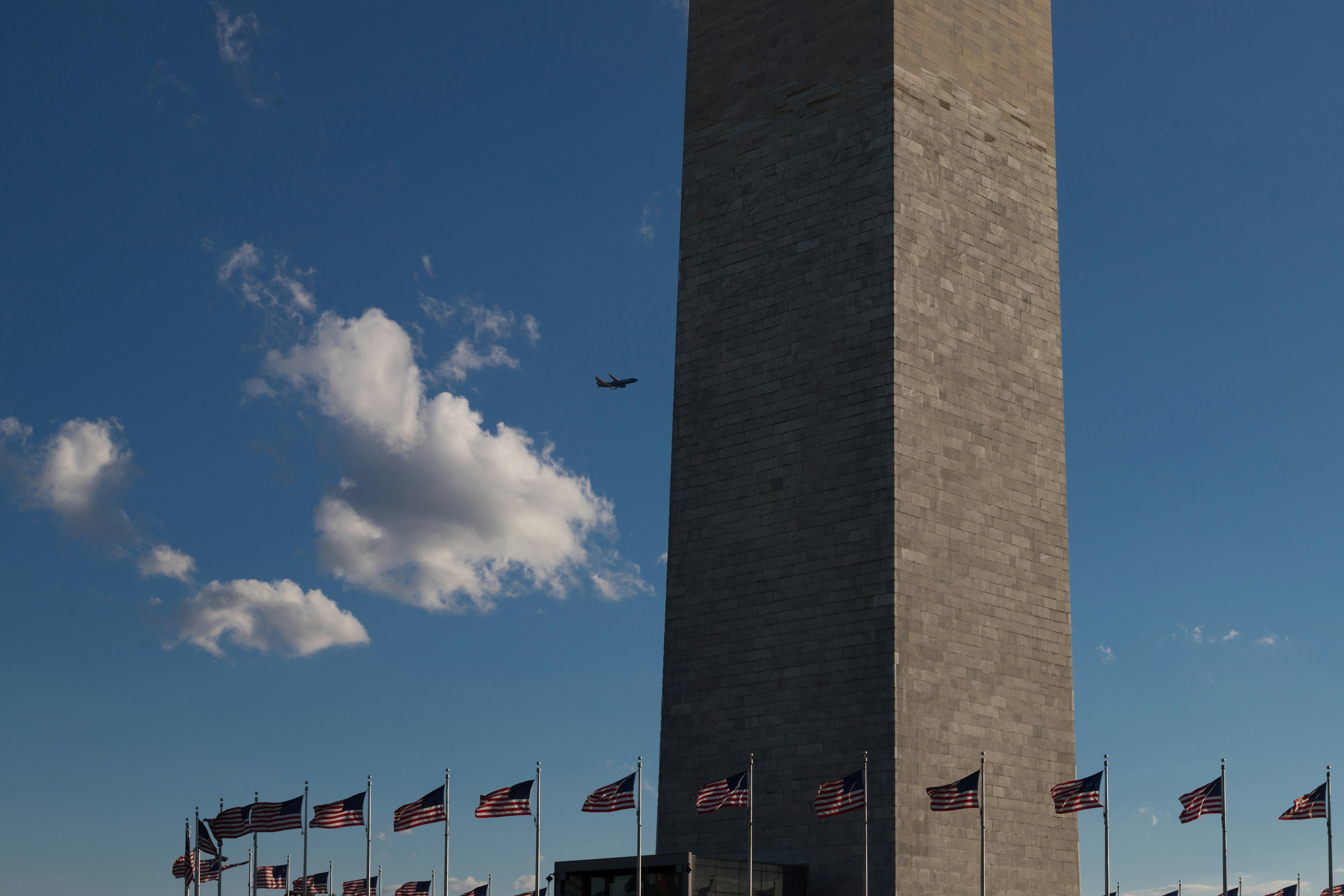 a plane flying over the washington monument with american flags