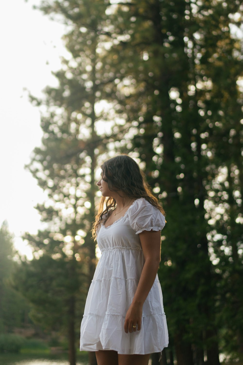 a woman in a white dress standing in front of trees