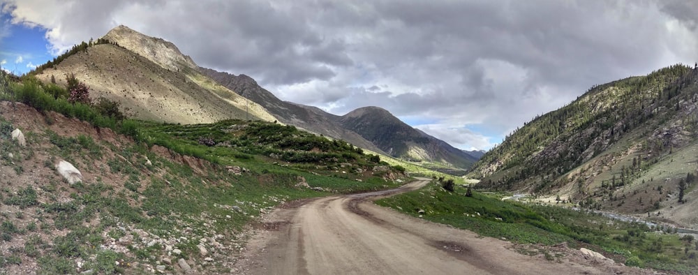 a dirt road surrounded by mountains under a cloudy sky