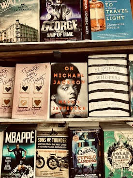 A bookshelf displaying various books including titles such as 'George and the Ship of Time', 'On Michael Jackson', and 'The Ghosts of Tupelo Landing'. The books are arranged in a tidy manner on wooden shelves.