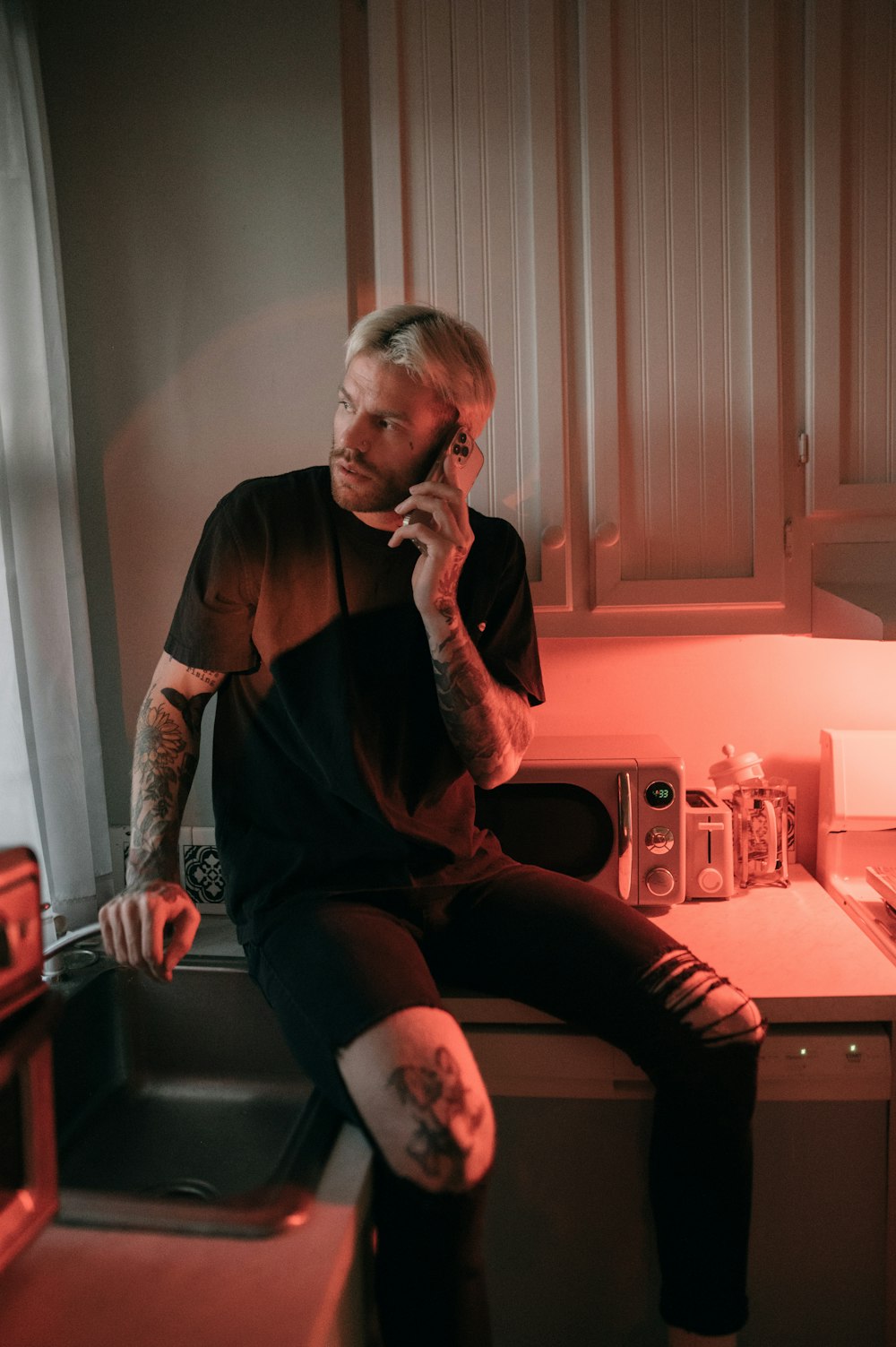 a man sitting on a kitchen counter talking on a cell phone