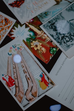 A collection of festive greeting cards, featuring colorful holiday designs and motifs. Some cards have Russian text, and one card prominently displays an illustration of Santa Claus next to an escalator. The images include decorations like ornaments and pine branches.