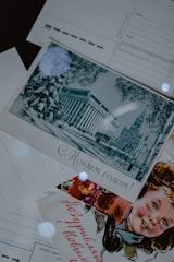 A collection of vintage postcards is displayed. One postcard features an illustration of an elegant building surrounded by winter scenery with trees. Another postcard displays a smiling child, possibly celebrating a festive occasion. The text on the postcards is written in Russian.