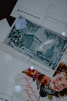 A collection of vintage postcards is displayed. One postcard features an illustration of an elegant building surrounded by winter scenery with trees. Another postcard displays a smiling child, possibly celebrating a festive occasion. The text on the postcards is written in Russian.