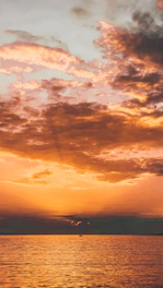 A vibrant sunset over the ocean with a small sailboat silhouetted against the glowing sky.