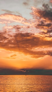 A vibrant sunset over a calm ocean with a small sailboat in the distance.