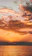 A vibrant sunset over calm bay waters with a small tour boat sailing nearby.
