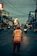 A happy man wearing a bright reflective vest standing on a city street at dusk.