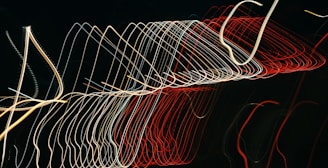 A series of multicolored light trails form abstract, curved patterns against a dark background, creating a dynamic and kinetic visual effect.