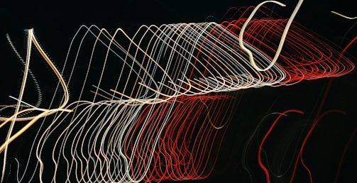A series of multicolored light trails form abstract, curved patterns against a dark background, creating a dynamic and kinetic visual effect.