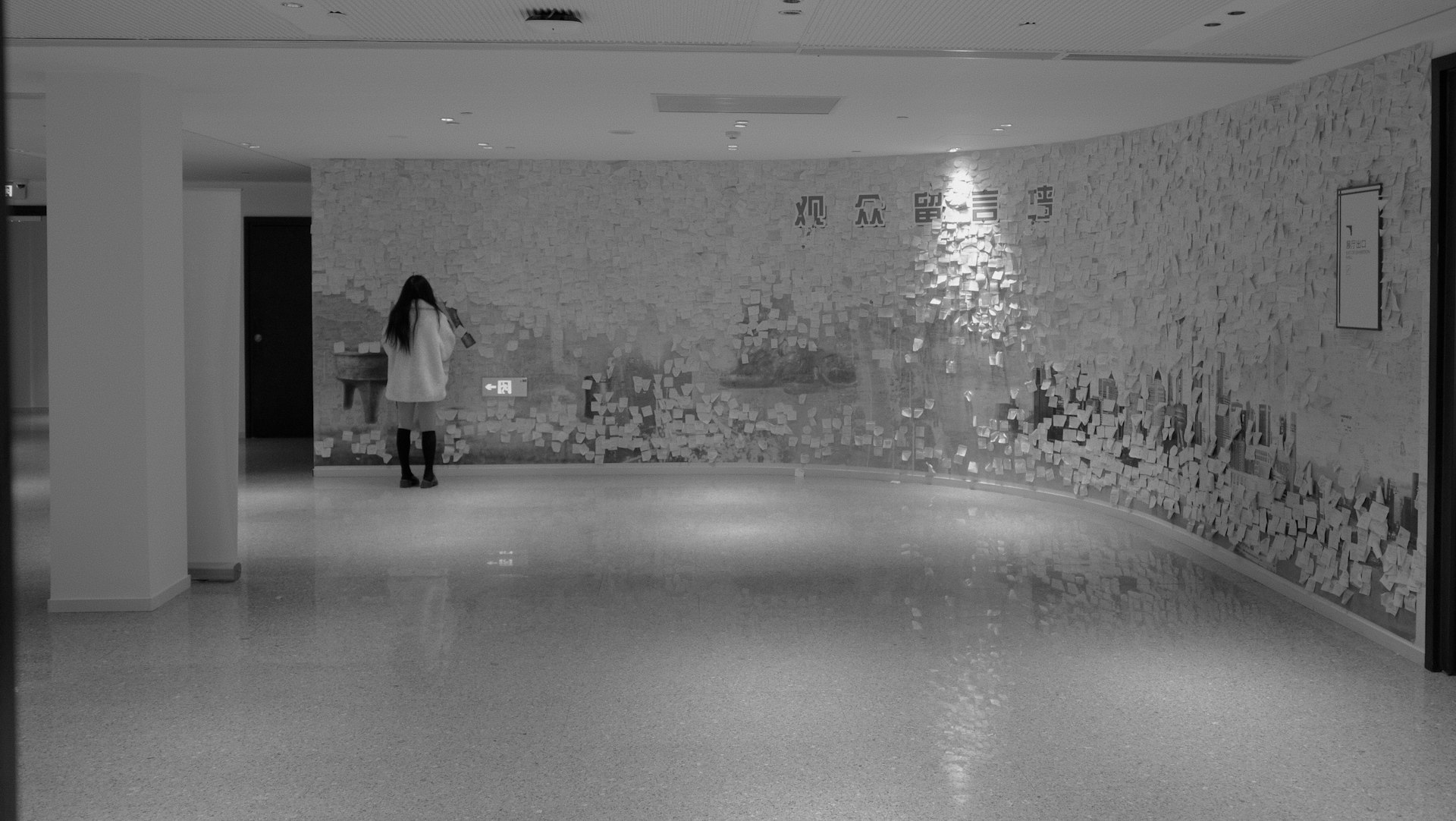 a black and white photo of a woman standing in front of a wall