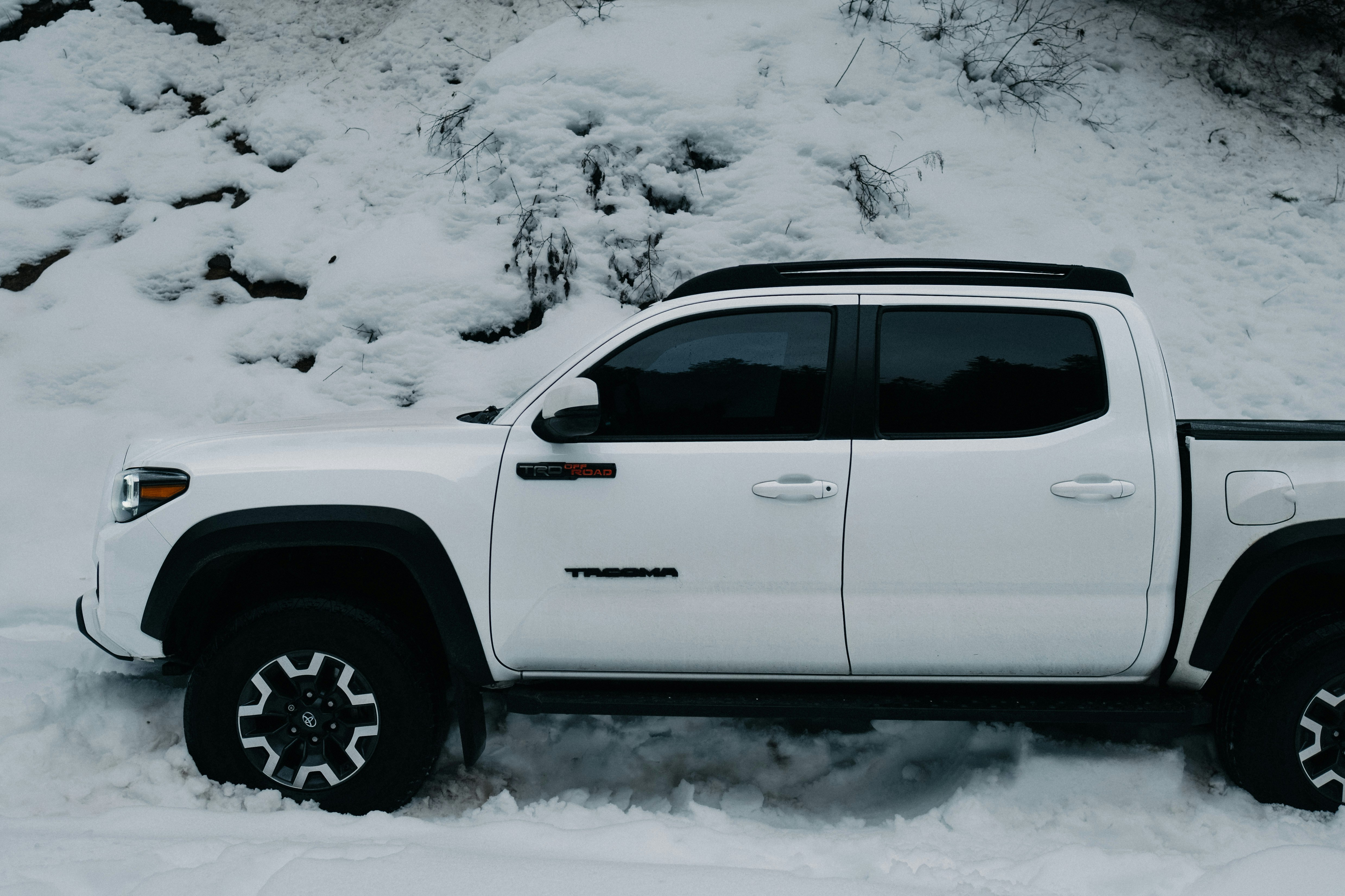 White pickup truck parked on a snowy hillside, foregrounded with tire treads and snowdrift, capturing a rugged outdoor moment.