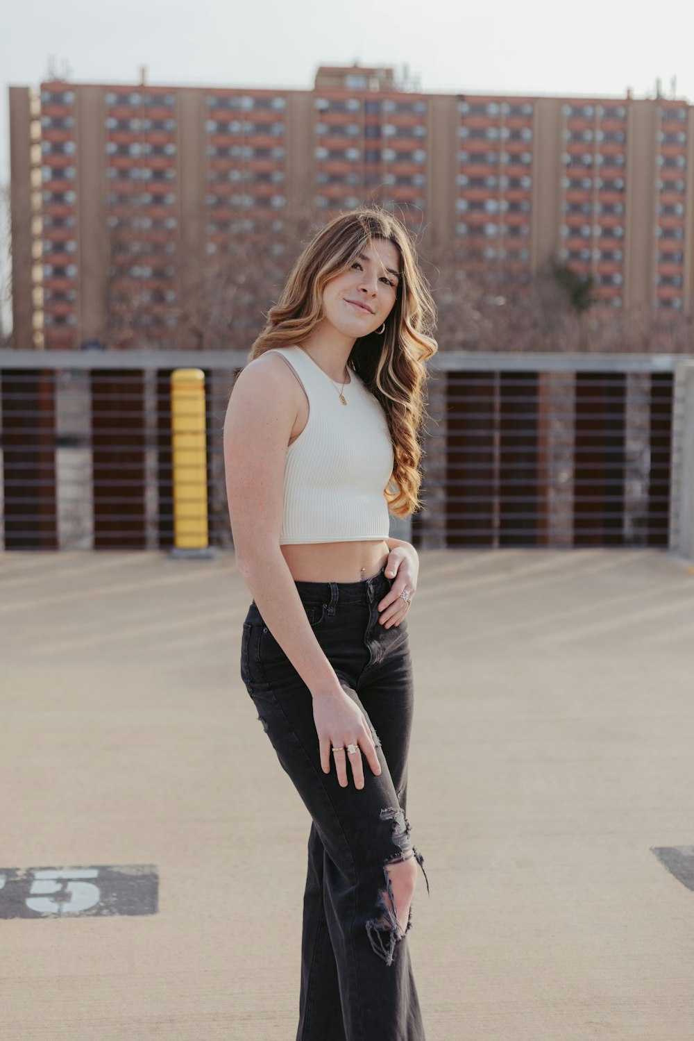 a woman standing in a parking lot wearing black pants and a white crop top