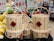 A stack of woven bamboo baskets with handles, displayed in a market. Each basket has a red diamond-shaped label featuring Chinese characters. Surrounding the baskets are signs indicating prices in various currencies and informational signage mostly in Chinese. To the left, there are green and yellow oversized pomelos, adding to the market setting.