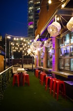 A cozy backyard setup featuring a sleek outdoor bar with stools and a beverage cooler under string lights.