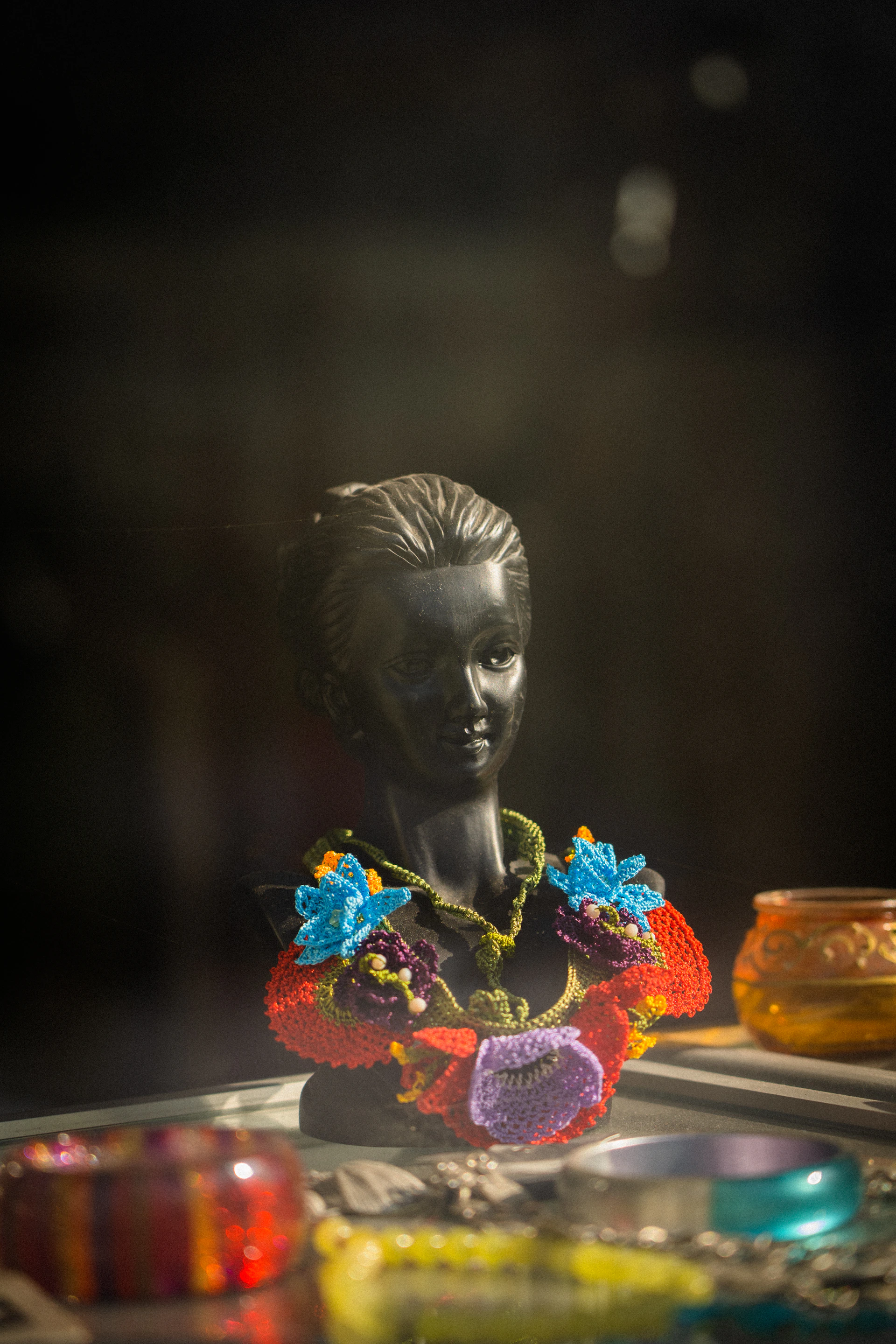 A vibrant necklace set crafted from molela terracotta clay displayed on a minimalist white bust, with natural light highlighting its earthy tones.