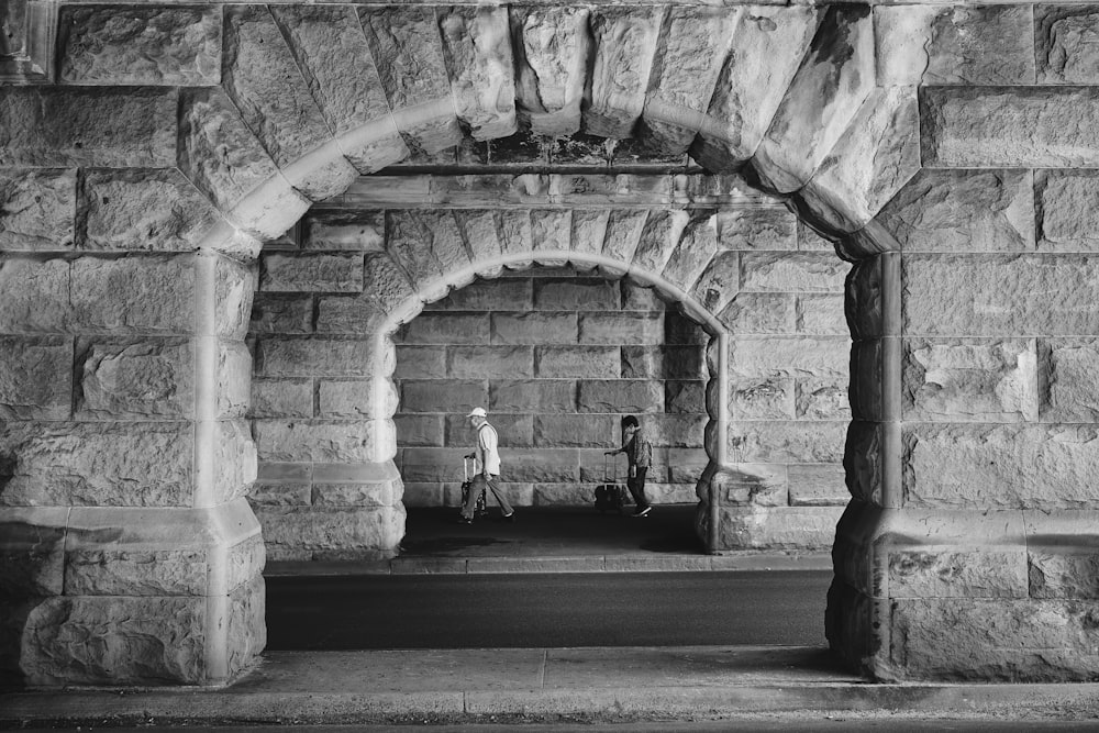 a black and white photo of two people standing in a stone archway