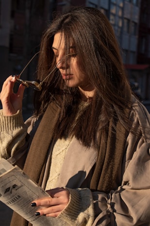A stylish woman wearing sophisticated glasses, smiling softly in natural light.