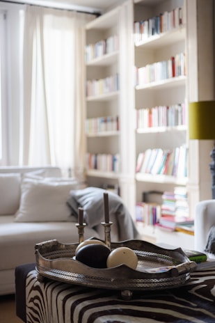 A cozy living room featuring a foldable storage ottoman in soft fabric next to a modular shelving unit filled with books and decor.