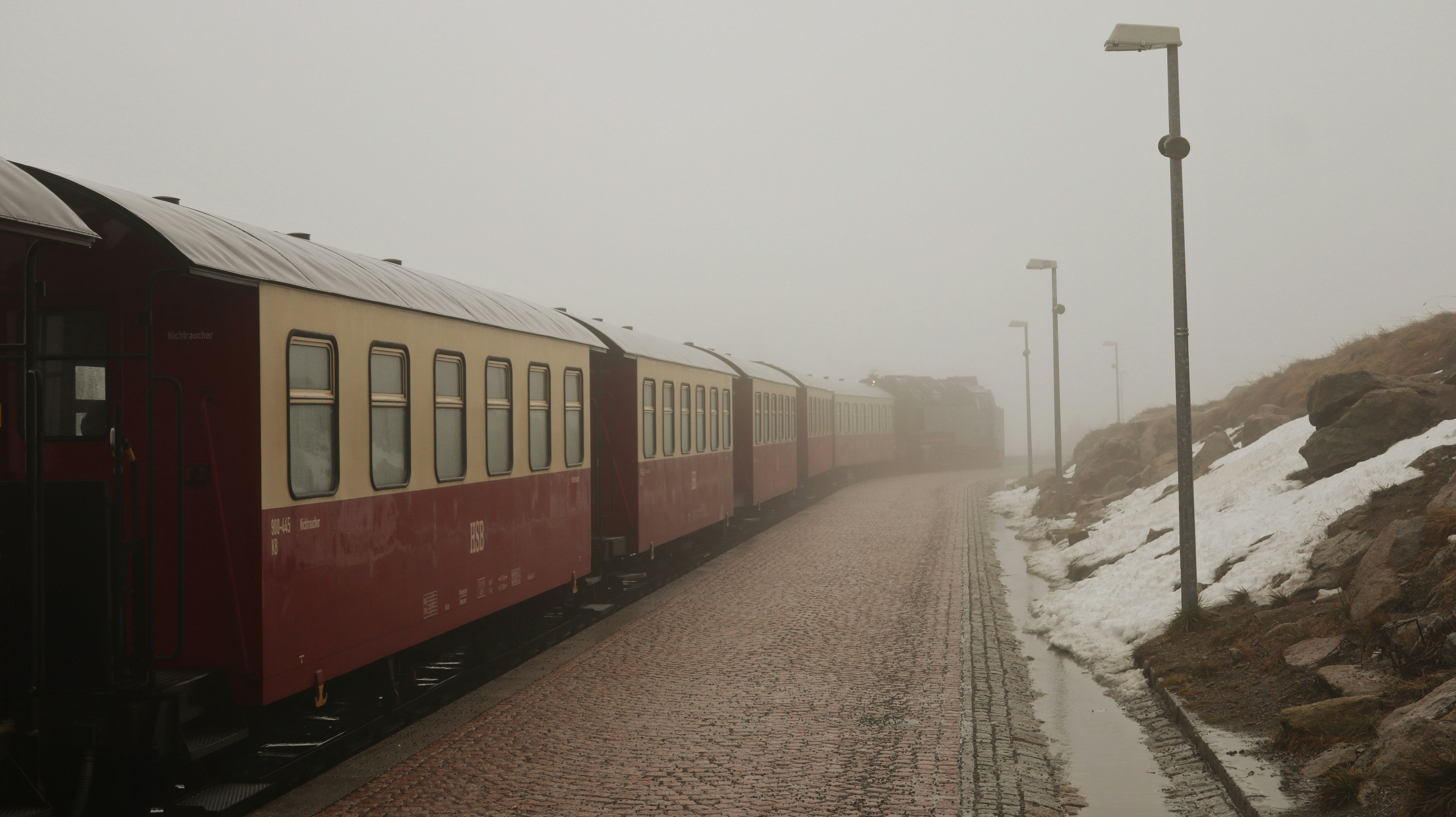 A red train traveling down train tracks next to a snow covered hillside ...