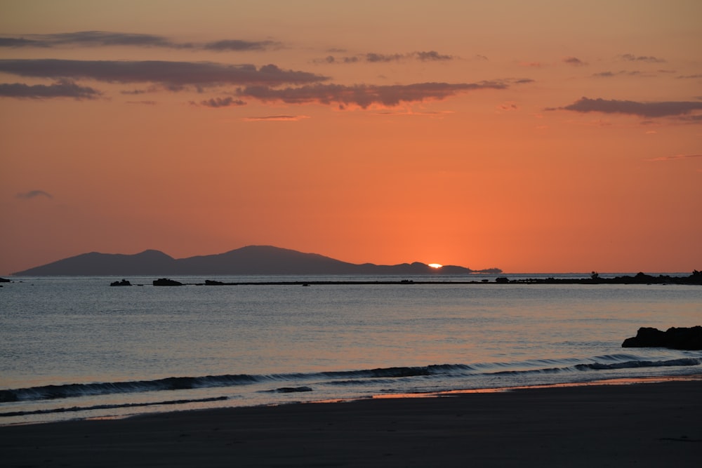 the sun is setting over the ocean with mountains in the distance