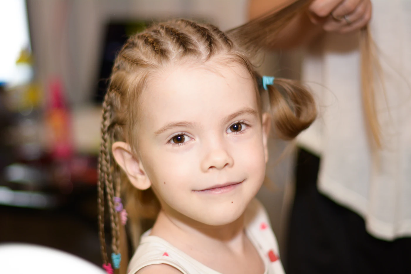 A stylist leaning in to comb and trim a small girl's hair while the girl looks up.