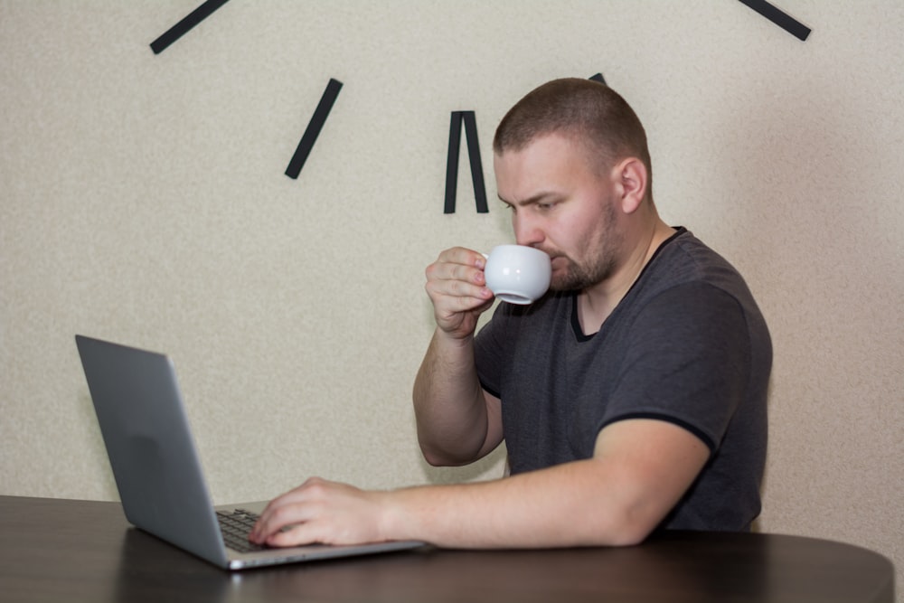 a man drinking a cup of coffee while using a laptop