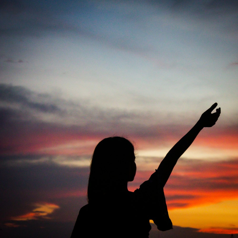a woman is silhouetted against a colorful sunset