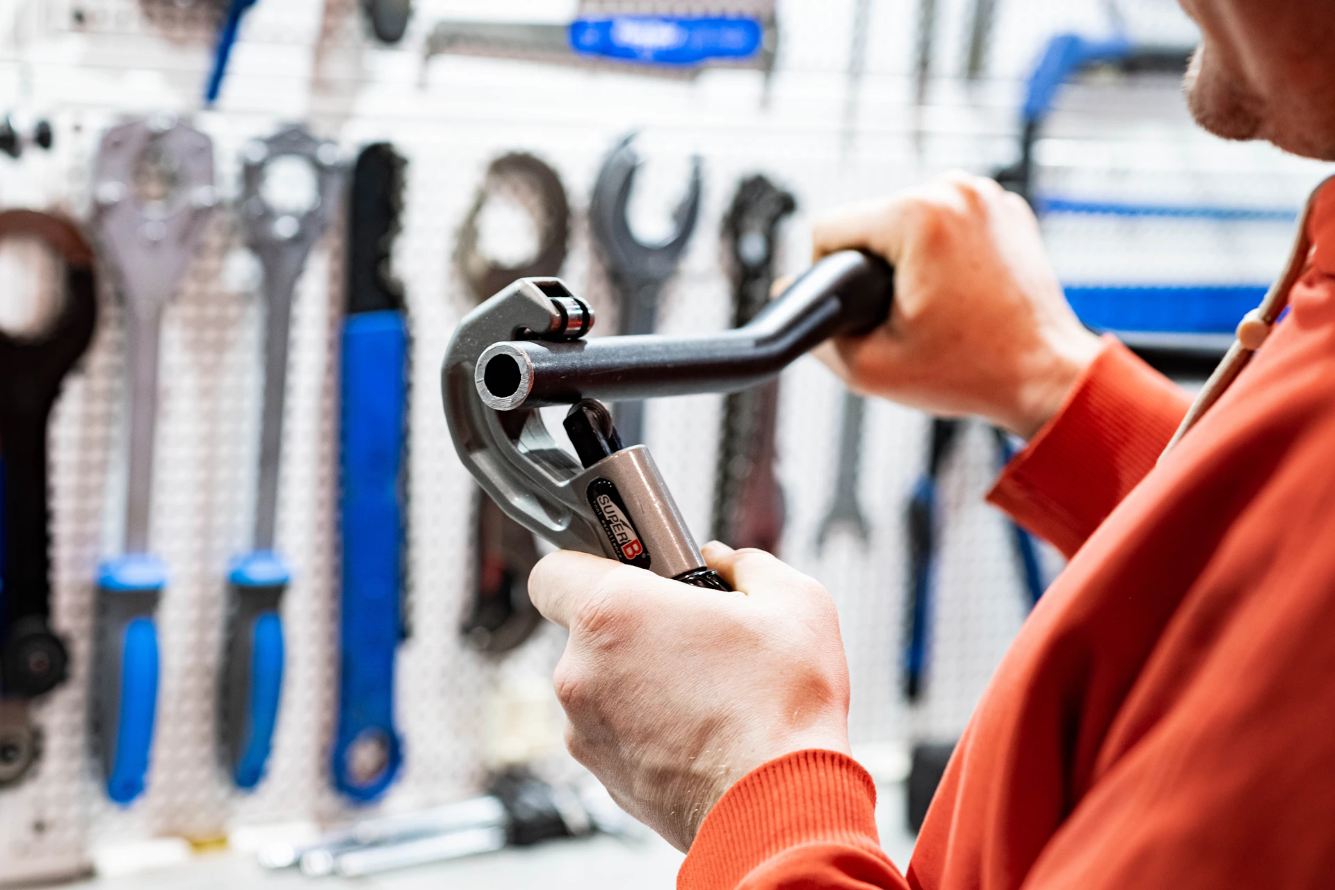 a man holding a wrench in front of a wall of tools