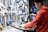 A person wearing a beanie and glasses works on a bicycle wheel, surrounded by an organized display of tools hanging on a pegboard. The person is using a spray bottle, likely for cleaning or lubricating the wheel.