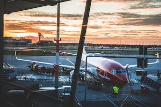 A sleek commercial aircraft taxiing on a runway at sunset with airport control tower in the background.