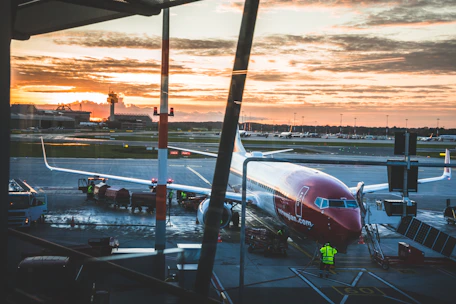 A sleek commercial aircraft taxiing on a runway at sunset with airport control tower in the background.