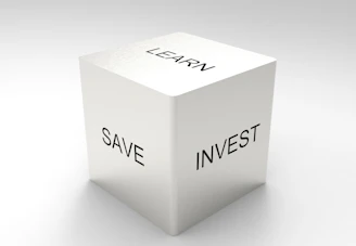 A three-dimensional cube with words on its visible sides, featuring 'LEARN' on the top, 'SAVE' on the left face, and 'INVEST' on the right face. The cube is rendered in a minimalist white and gray color palette, creating a clean and professional look.