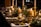 A beautifully set dining table with elegant candles, gold candlesticks, and lush greenery. Rolled white napkins and gold cutlery complement the luxurious atmosphere, while soft lighting enhances a sophisticated ambiance.