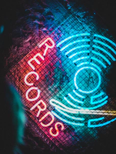 Vibrant neon lights form the word 'RECORDS' alongside a circular, radiating pattern on a textured, dark background. The glowing text is in bright red, contrasting with the blue and teal neon elements that resemble sound waves or records.