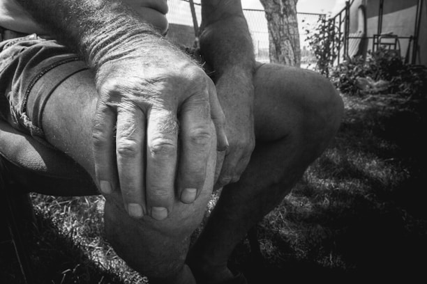 Close-up of a person gently massaging their knee outdoors.