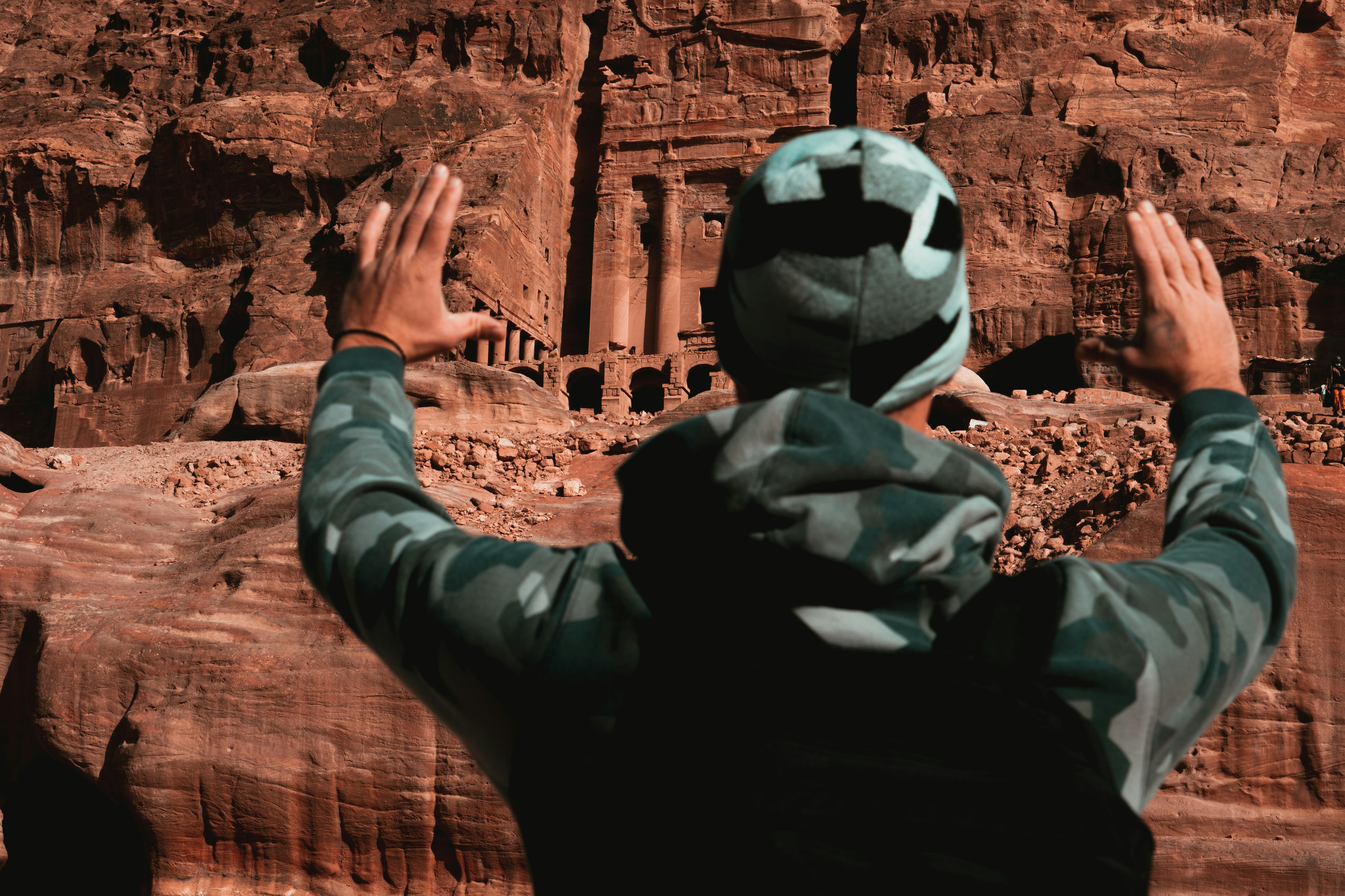 A man in camouflage jacket standing in front of a rock formation photo ...