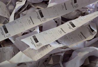 A cluttered desk covered with piles of receipt paper and invoices.