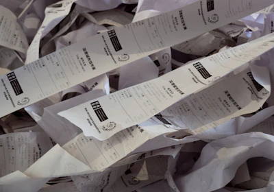 A cluttered desk covered with piles of receipt paper and invoices.