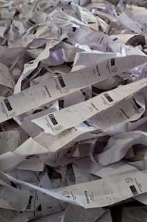 A chaotic pile of crumpled and twisted paper receipts, forming a dense heap. Each receipt has printed text and barcodes visible on some parts. The papers are randomly intertwined, creating a cluttered and messy appearance.