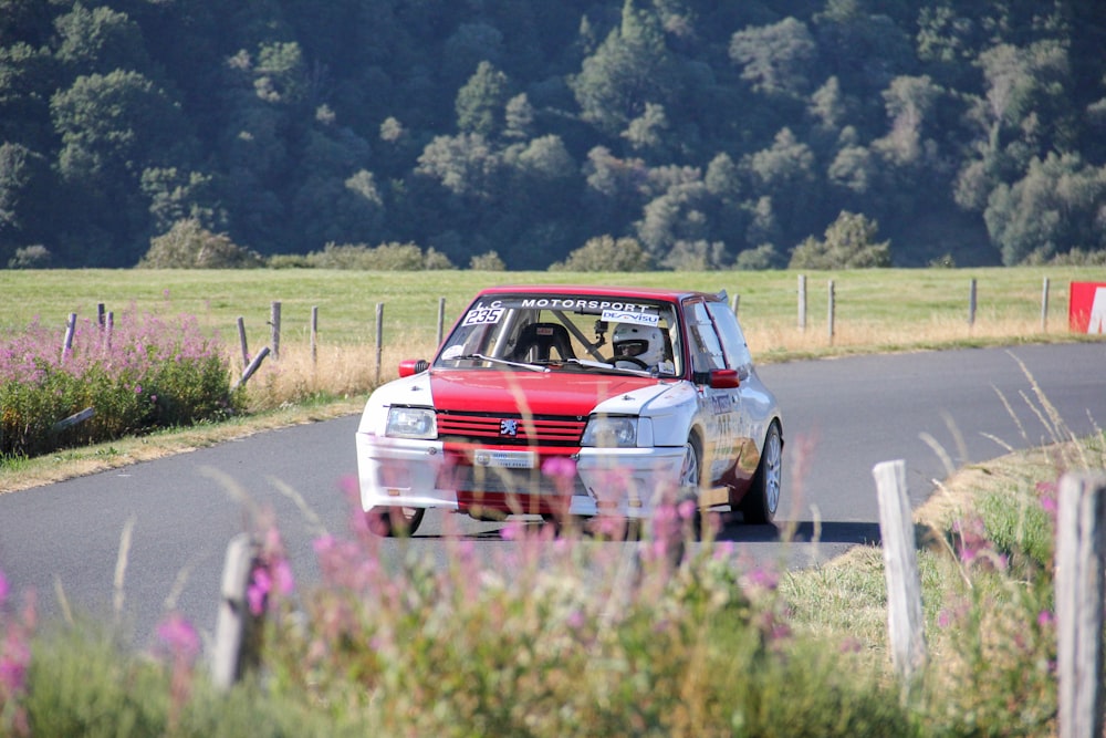 a red and white car driving down a country road