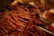A collection of cured sausages is arranged on a surface, with strings attached for hanging. The background includes packaged meats and has a warm, dim lighting that emphasizes the textures.