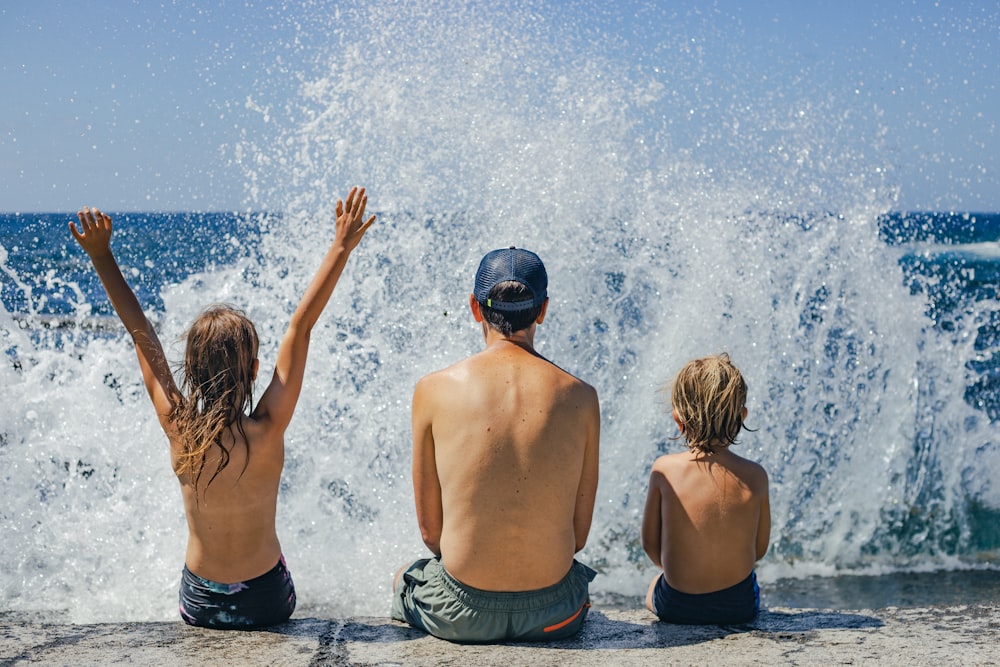 a couple of kids sitting on top of a beach next to the ocean