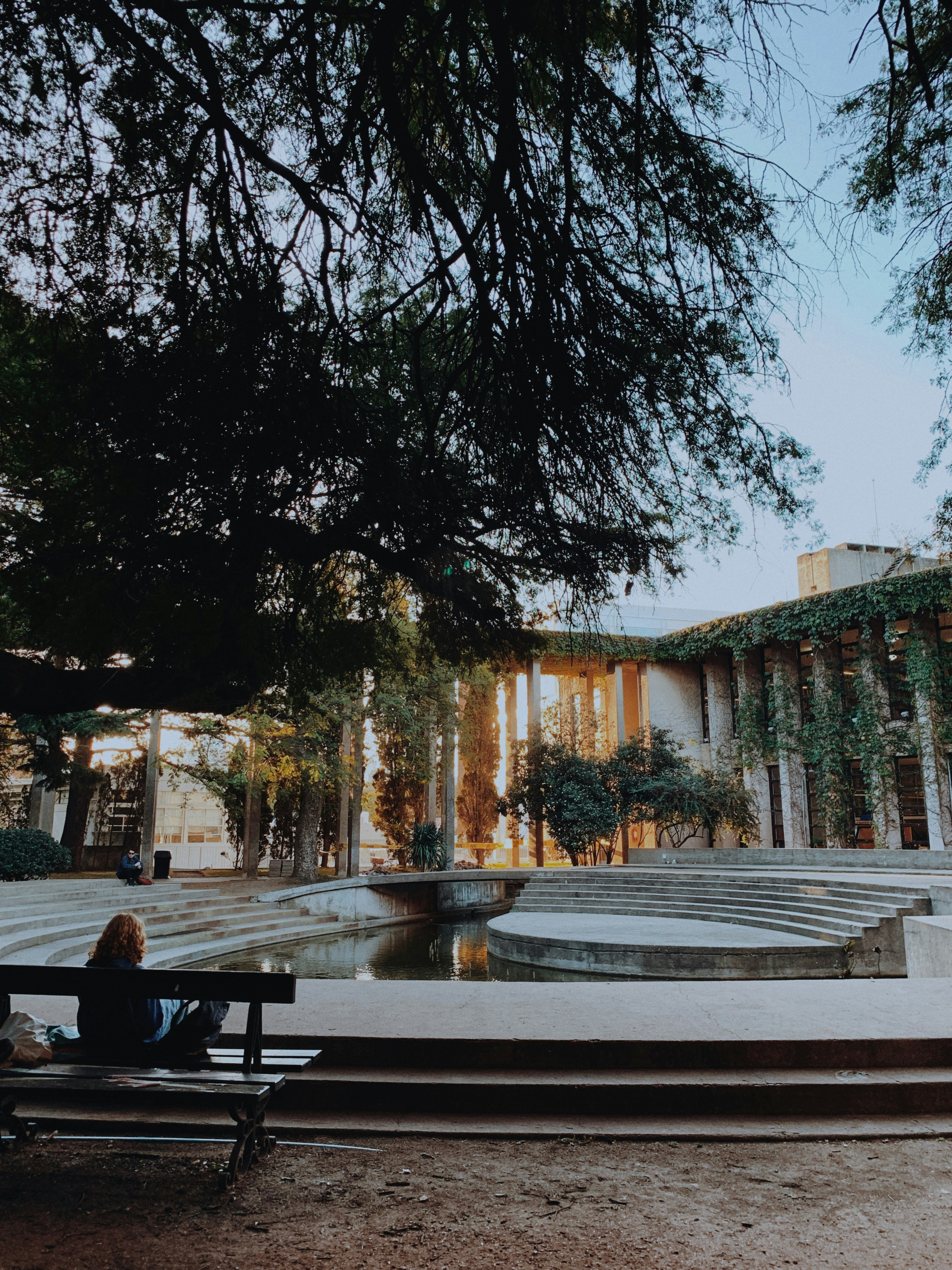 A woman sitting on a bench in front of a building photo – Free Urban ...