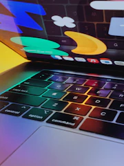 A close-up of hands typing on a keyboard with a blue and golden orange color scheme reflected on the screen.