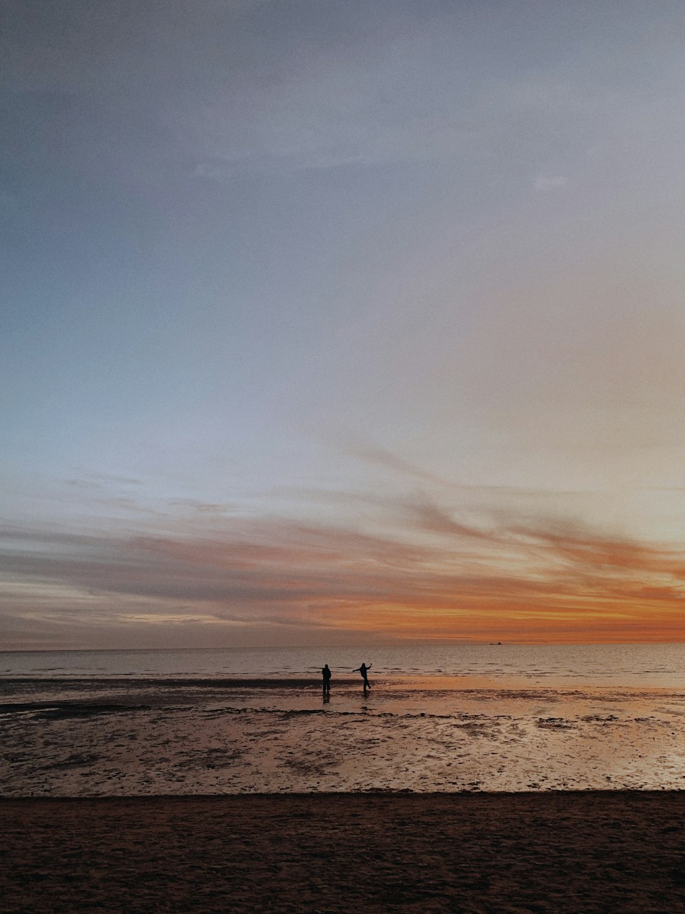 a couple of people standing on top of a sandy beach