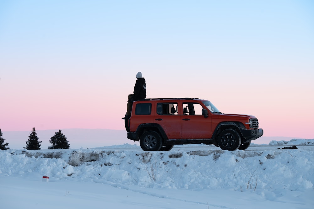 a person standing on top of a red vehicle in the snow
