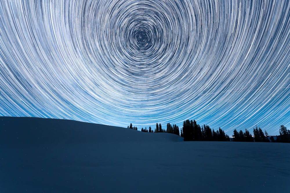a star trail in the sky over a snow covered hill