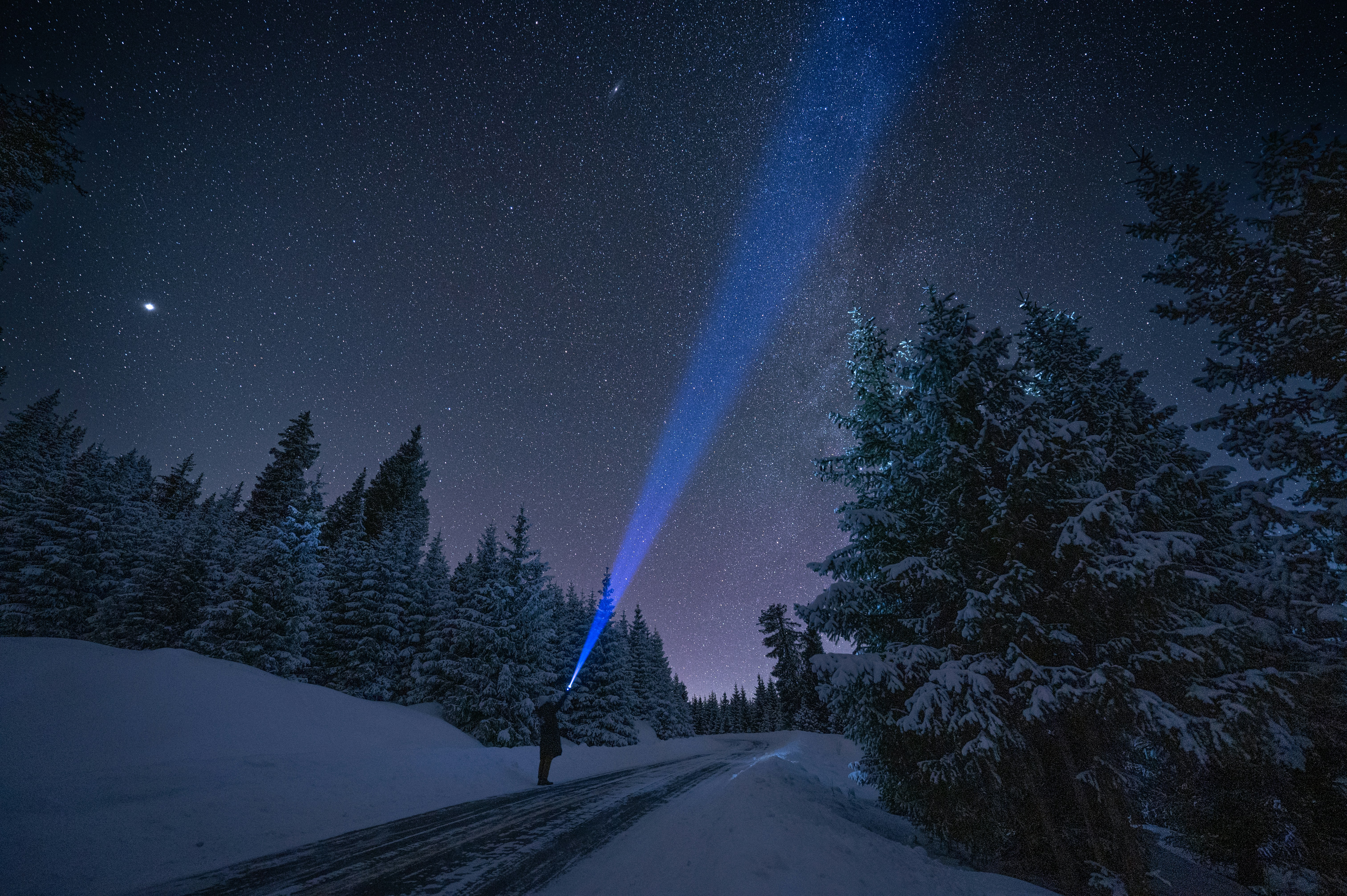 a person standing on a snow covered road under a sky full of stars