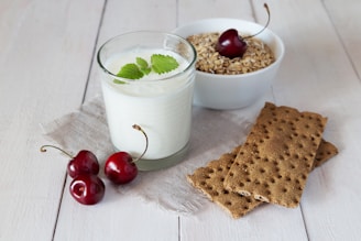 a glass of milk, crackers and cherries on a white table